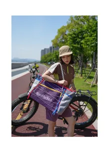 Outdoor cycling travel bag detail showing model wearing purple drawstring shoulder bag in park setting.