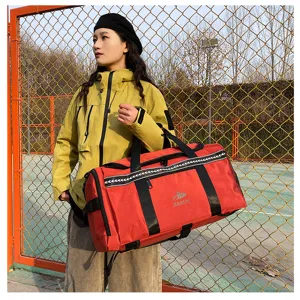 Outdoor detail shot of a large red duffel bag with black straps and white trim held by model.
