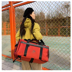 Outdoor detail shot of a red travel duffel bag with black straps being worn by a model.