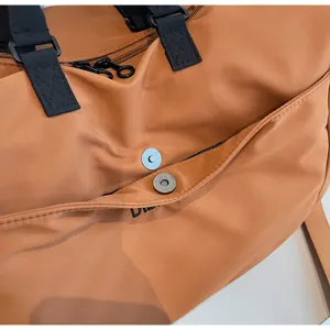 Detail view of a large capacity brown travel duffel bag with black straps and snap button.