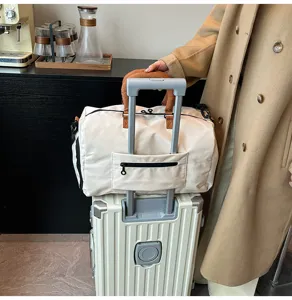 Details of beige travel duffel bag with brown handles and luggage strap on suitcase.