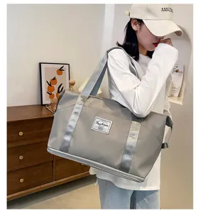 Grand sac de voyage gris avec des sangles argentées et un compartiment zippé inférieur.