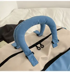 Close-up detail of travel bag handle and dual zippers, soft padded blue and beige fabric.