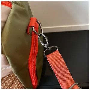 Close-up detail of durable travel bag hardware, metal clasp hook and adjustable orange strap.