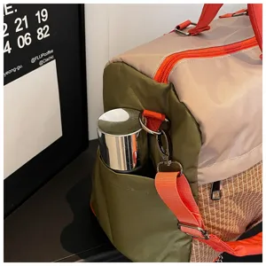 Close-up detail of travel duffel bag side pocket with metal bottle and orange straps.