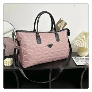 Vue détaillée du sac de voyage matelassé rose avec texture géométrique et poignées noires.