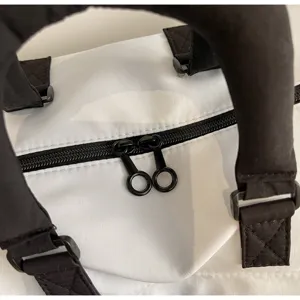 Close up detail of white travel duffel bag with black handles and double zippers.