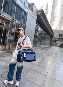 Large capacity blue travel duffel bag with shoulder strap and cute bear pendant in outdoor scene.