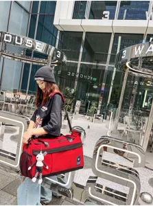 Detailed view of the red and black travel duffel bag worn in urban lifestyle setting.