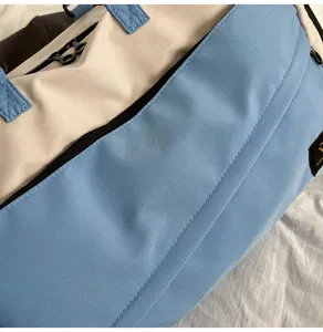 Close-up detail of color-blocked travel duffel bag in light blue and cream fabric.
