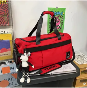 Red and black casual travel duffel bag with crossbody strap and cute doll pendant.