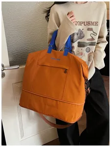 Detail view of large orange travel duffel bag with blue handles and front pocket.