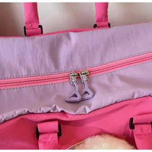 Vue de détail du sac de voyage rose et violet avec doubles fermetures éclair et tirettes.