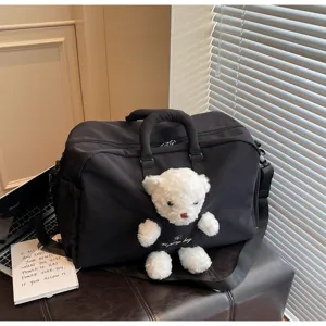 Détail de sac de voyage noir avec pendentif en peluche blanche et bandoulière robuste.