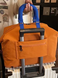 Orange travel duffel bag with blue handles and trolley sleeve for convenient luggage storage.