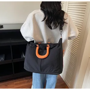 Stylish black travel bag with orange handles, large capacity messenger bag for daily trips.