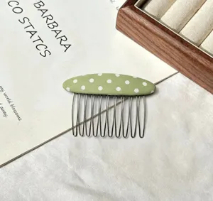 Close-up of a stylish green polka dot hair comb with metal teeth for styling bangs and hair.