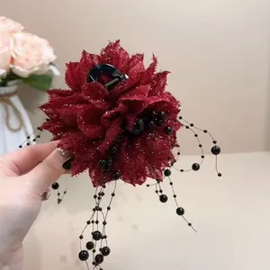Vue détaillée de la pince à cheveux fleur en tissu rouge foncé avec franges de perles.