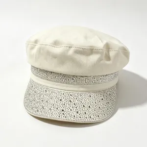 Vista dettagliata di un elegante berretto piatto bianco sporco decorato con brillanti strass.