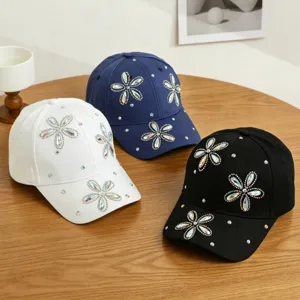 Detailopname van sprankelende strass-bloem versierde honkbalpetten in wit, blauw en zwarte kleuren.