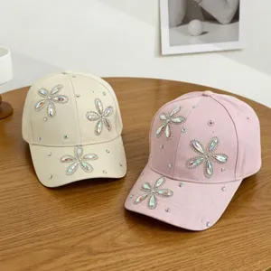 Gedetailleerd uitzicht op kinderbaseballpetten met iriserende strassbloemen in beige en roze.