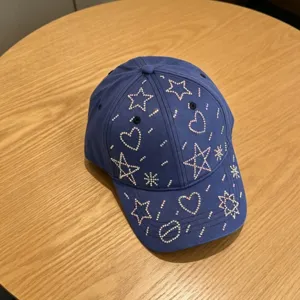 Detailopnames van de blauwe honkbalpet met fonkelende strass-sterren en hartjes erop.