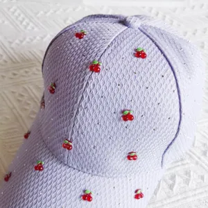 Close-up detail of lavender waffle baseball cap with sparkly rhinestones and cute red cherries.