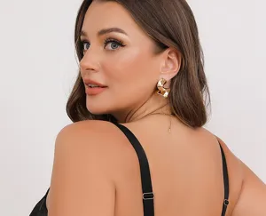 Primo piano di eleganti orecchini in metallo torto e dettaglio di bretelle di lingerie.