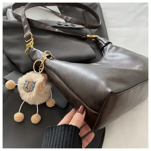 Brown retro hobo dumpling bag with cute plush pendant, casual commuter shoulder bag style.