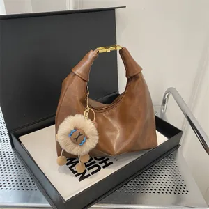 Brown faux leather dumpling shoulder bag detail showcasing fluffy plush charm and gold buckle.