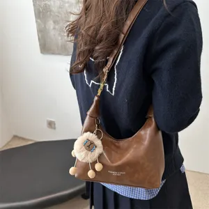 Brown leather hobo shoulder bag detail featuring cute plush charm and minimalist daily style.