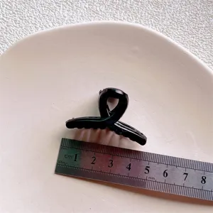 Mini black hair claw clip detail close-up showing compact size and sleek glossy plastic design.