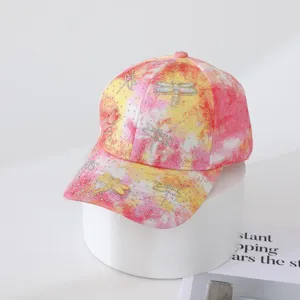 Detail view of colorful tie-dye baseball cap featuring sparkly rhinestone dragonfly embellishments.