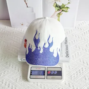 Detail view of a white baseball cap featuring striking blue rhinestone flame patterns, street style.