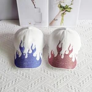 Detailed close-up of white baseball caps featuring sparkly rhinestone flame patterns.