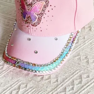 Detalle en primer plano del borde de la gorra de béisbol con mariposa de diamantes rosa.