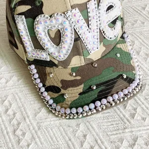 Camo baseball cap detail with sparkling rhinestone pearls and white love patch design.