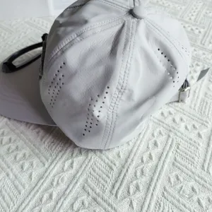 Grey quick-dry baseball cap detail shot, featuring breathable ventilation holes and strap.