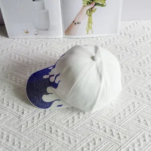 Streetwear style white baseball cap featuring striking blue rhinestone flame design on brim.