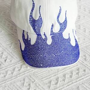 Close-up view of a white baseball cap featuring sparkling blue rhinestone flame patterns.
