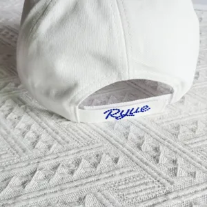 Detailed view of white baseball cap with blue rhinestone back strap letter. Streetwear style.