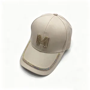 Close-up detail of beige baseball cap with rhinestone M logo and sparkling brim trim.