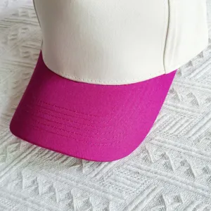 Close-up detail of a stylish two-tone baseball cap featuring a white crown and pink curved brim.