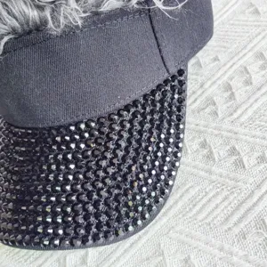 Close-up view of the black visor brim covered in sparkly rhinestones and grey hair.