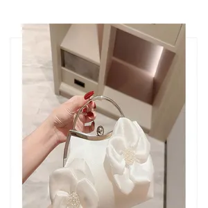 Detailed view of white satin evening bag with floral appliqués and metal handle for events.