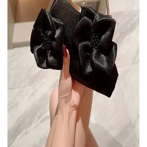 Close-up detail of black satin evening clutch bag with elegant fabric flower appliques.