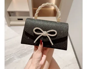 Gros plan d'un sac de soirée noir pailleté avec nœud en strass et poignée en cristal.