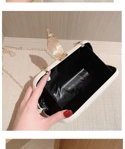 Elegant evening clutch bag detail showcasing golden feather clasp and chain strap.