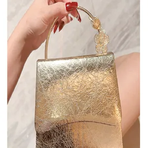 Close-up of gold cracked leather evening bag with metallic round handle and rhinestone flower.