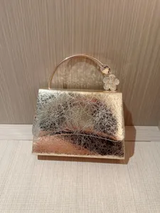 Gold metallic leather evening clutch bag with elegant rhinestone flower handle for party.